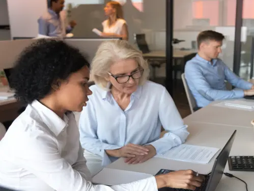 Grey-haired woman helps younger woman at computer