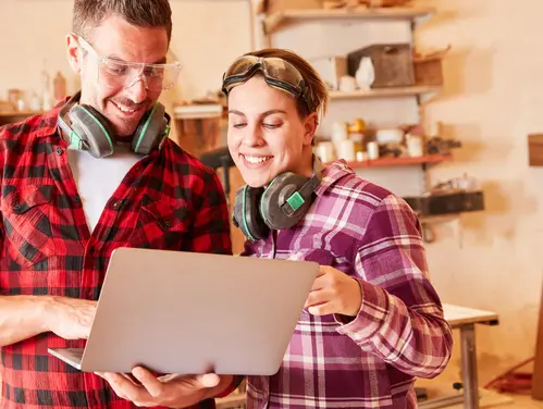 two smiling people looking at construction plans