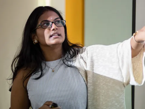 A woman in front of a white board teaching a course.