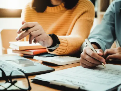 Photo of two people sitting down with paperwork and applying for something.