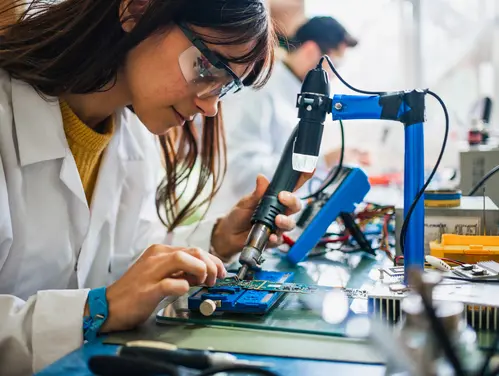 A photo of a woman in a work-based learning experience and working on a circuit board.