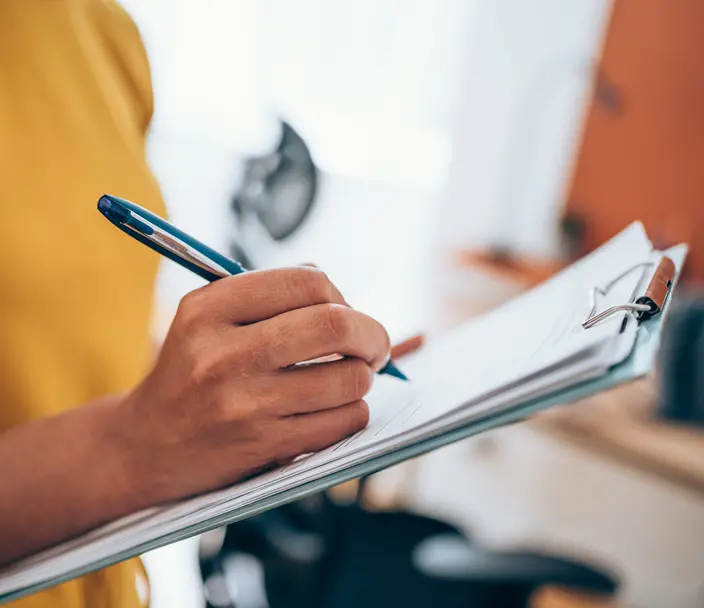 A person writes on a checklist with a pen.