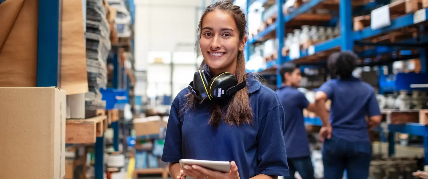 Woman smiles at the camera while she is working at a warehouse.