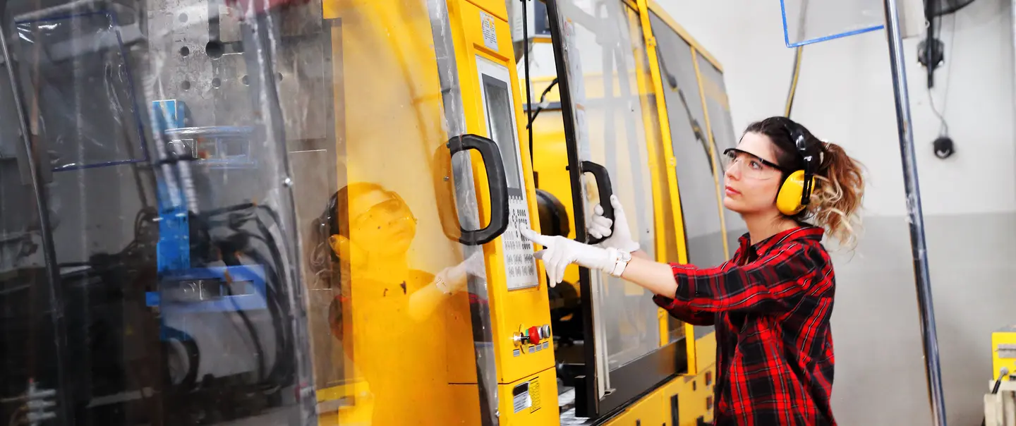 A woman operates a machine at an advanced manufacturing plant.