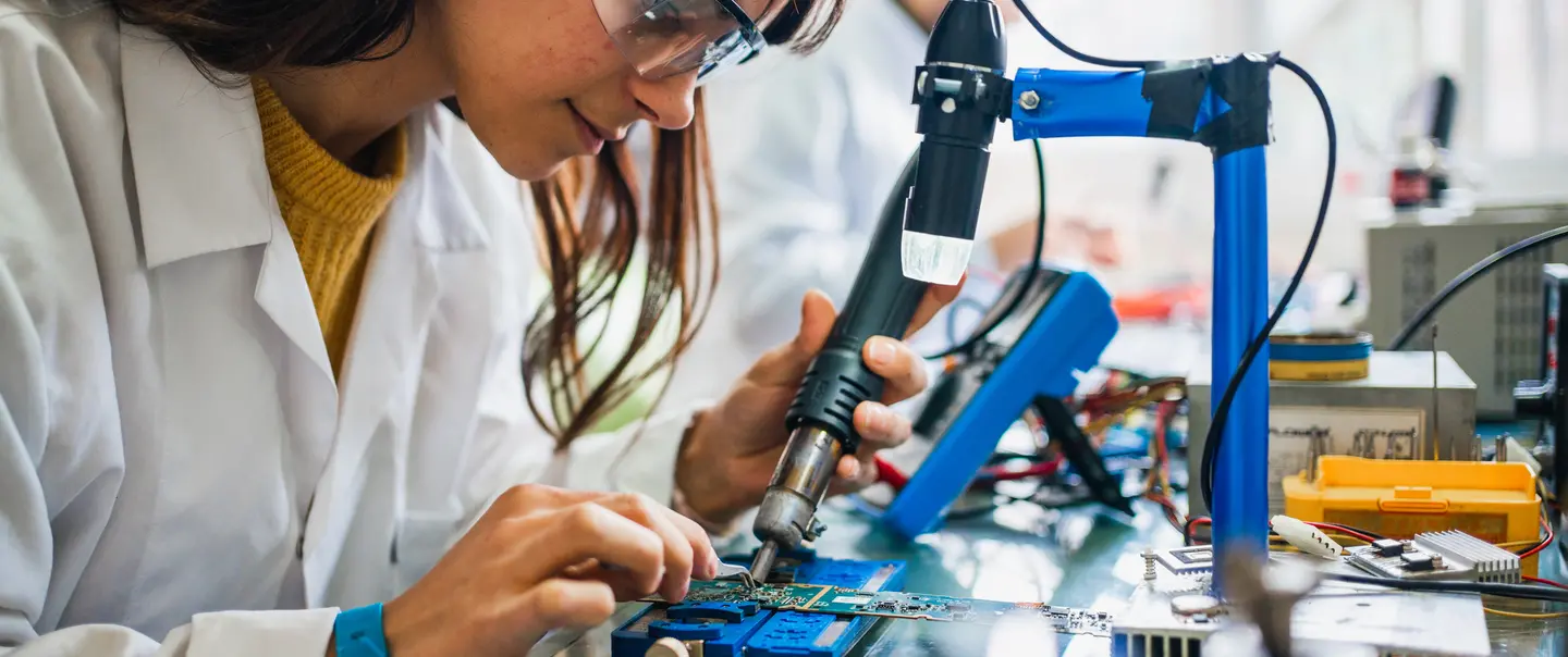 A photo of a woman in a work-based learning experience and working on a circuit board.