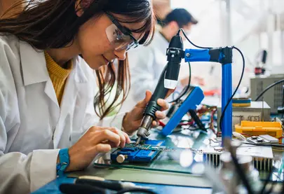 A photo of a woman in a work-based learning experience and working on a circuit board.