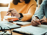 Photo of two people sitting down with paperwork and applying for something.