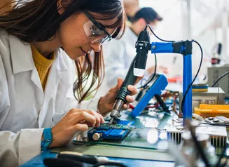 A woman in a work-based learning experience and working on a circuit board.