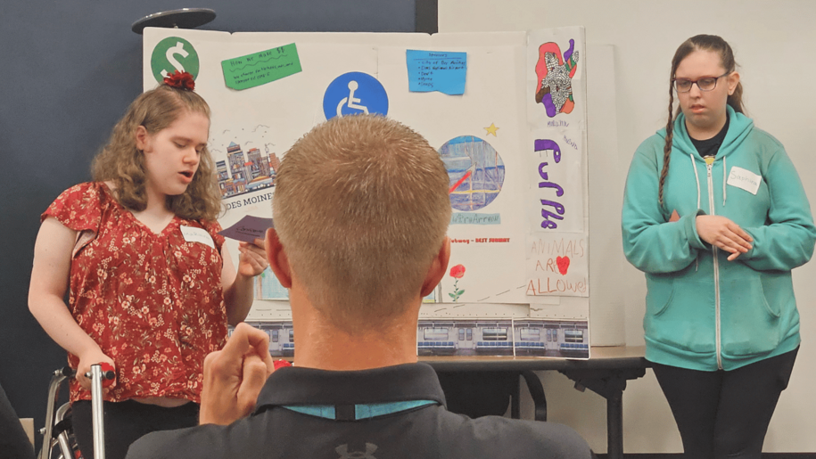 Two program participants in the Pre-Employment Transition Services (Pre-ETS) stand and give a presentation during the "Shark Tank" portion. They both helped create a cellphone idea that would be charged by walking and are presenting their idea to a business leader.