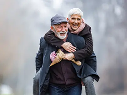 older man giving piggyback ride to older woman